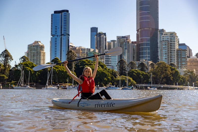 Lady kayaking on the Brisbane River, with her paddle above her head