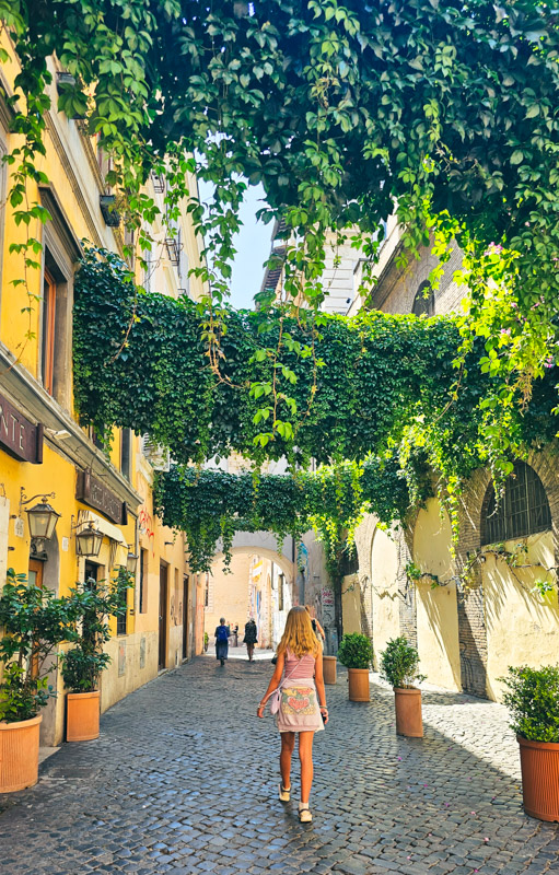 girl walking under vines hanging across street in Trastevere