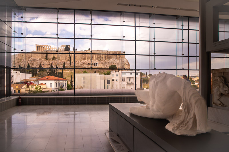 statue lying on museum display with acropolis views outside the wall to floor glass windows