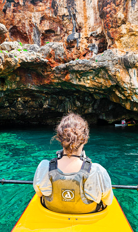 girl in kayak looking at sea cave entrance