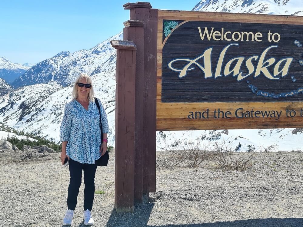 person beside welcome to alaska sign