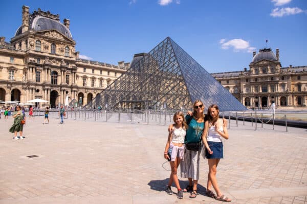 Mom and two daughters in front of a glass pyramid at the Louvre Museum in Paris