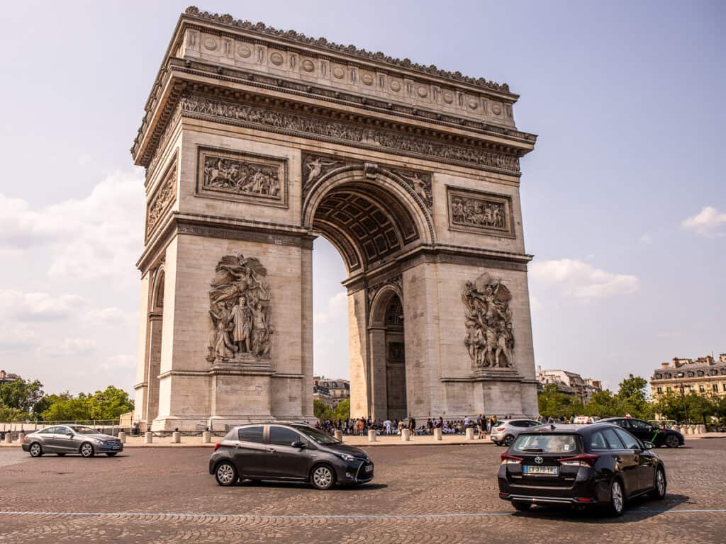 Cars driving around a large arch monument called the Arc De Triomphe