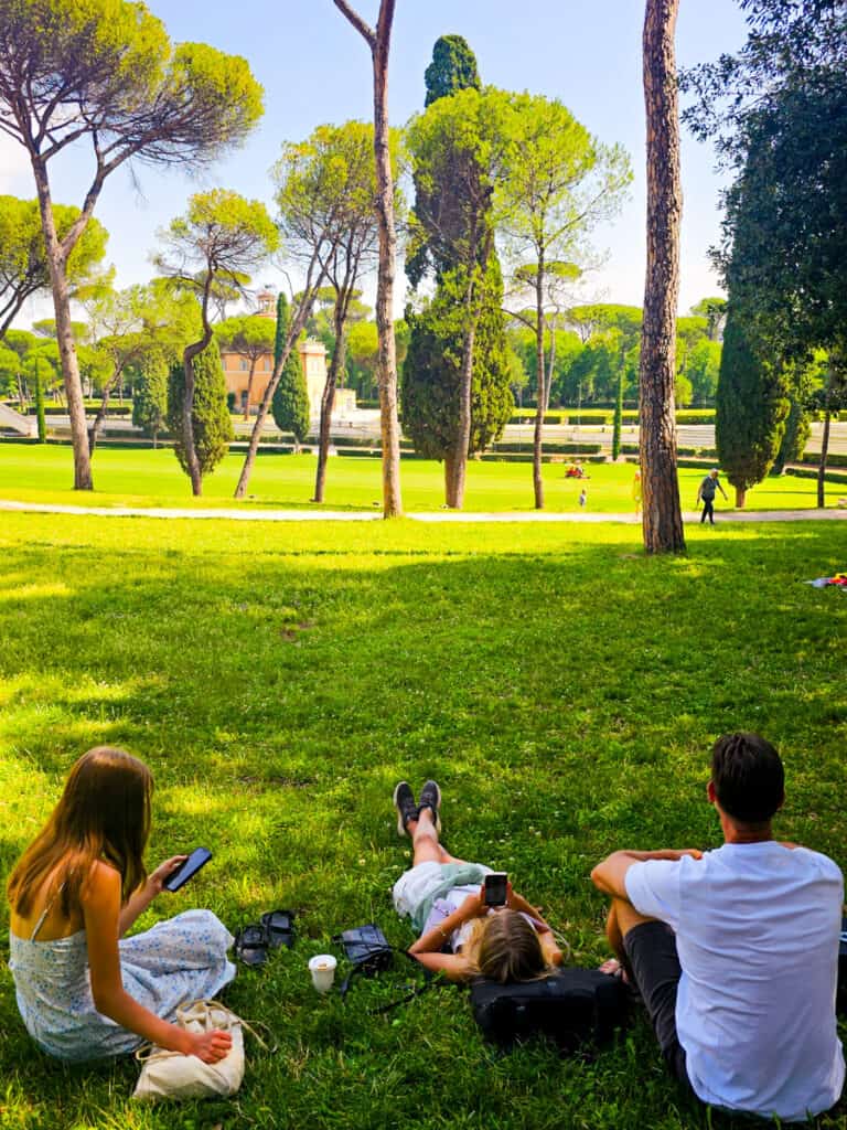 craig and girls sitting on grass looking at phones in the borghese Gardens