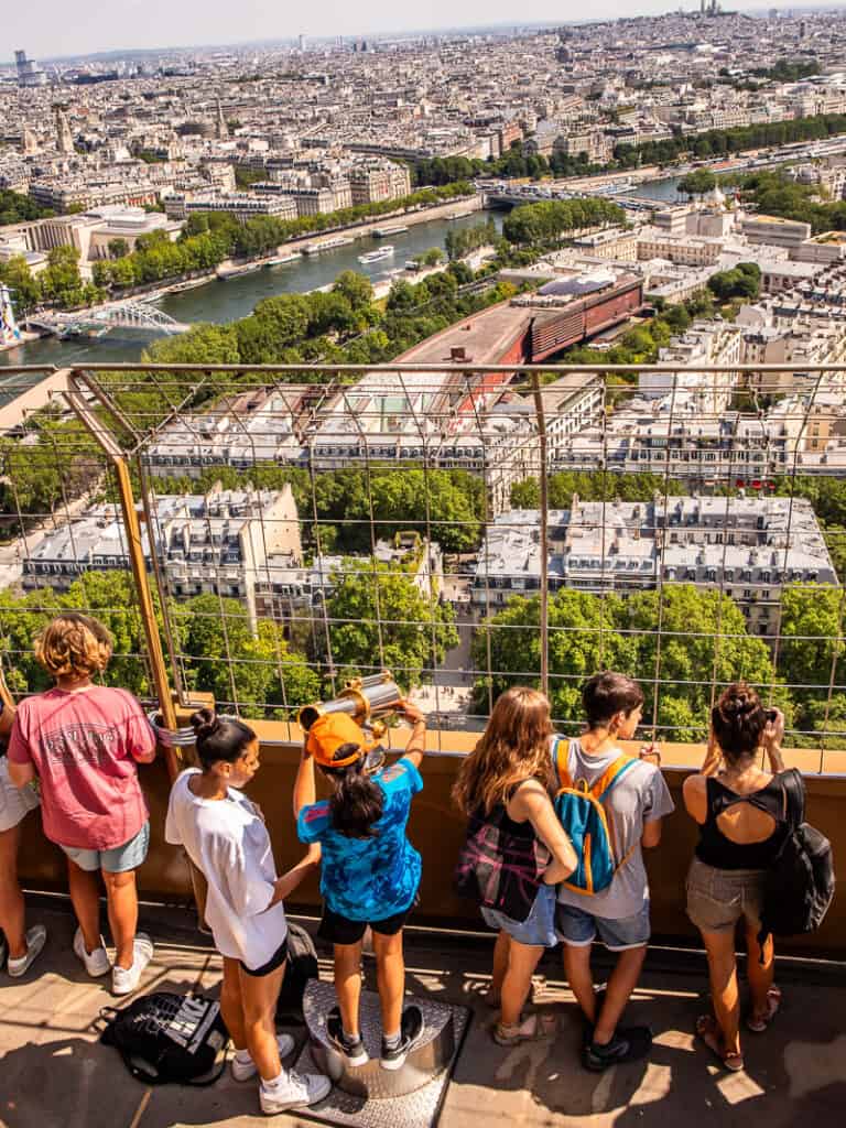People looking through a wire fence over Paris from the Eiffel Tower
