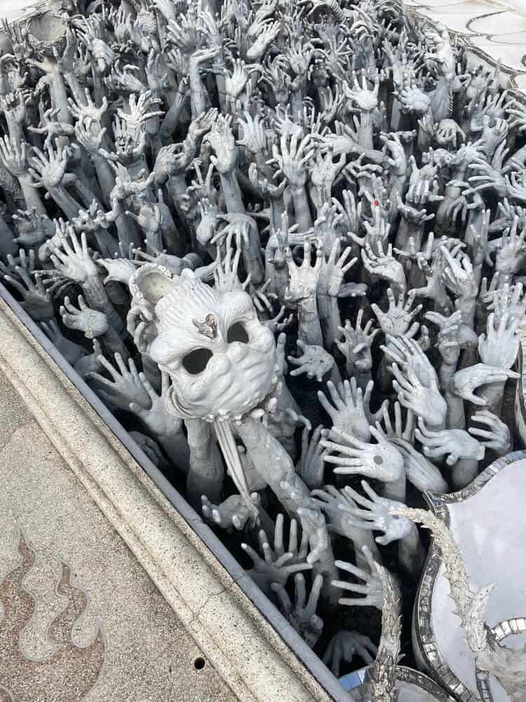 hundreds of marble hands in hole in ground raising up a skull