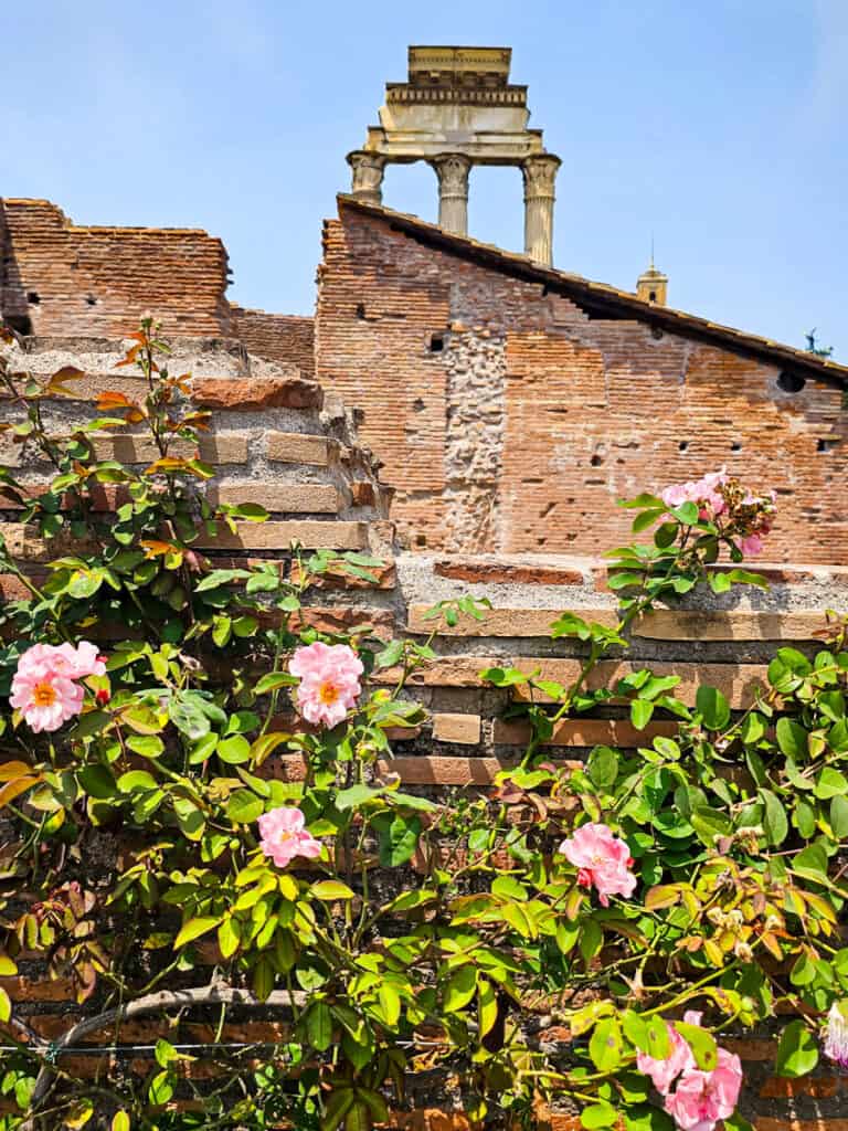 top of a temple as seen over a brick wall with pink flowers in front