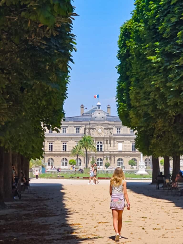 savannah walking down tree lined path with luxembourg palace in front of her