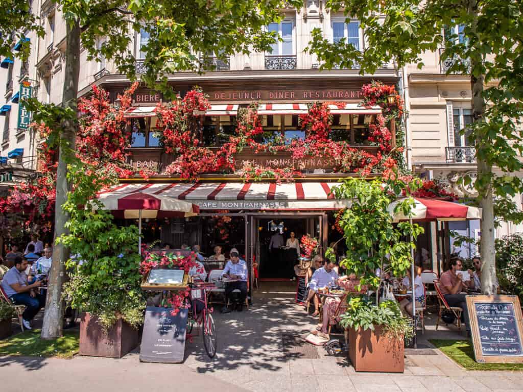 People sitting outside the flower draped Montparnasse cafe 