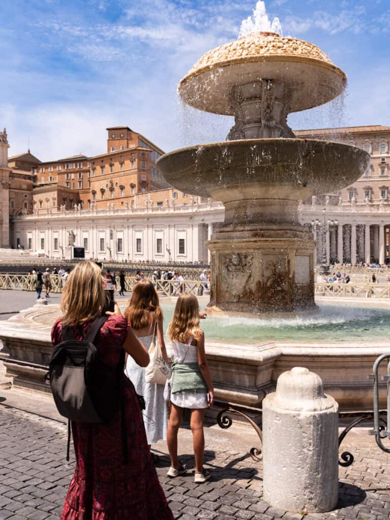 woman taking photo of two girls looking at water fountain in St Peter's Square