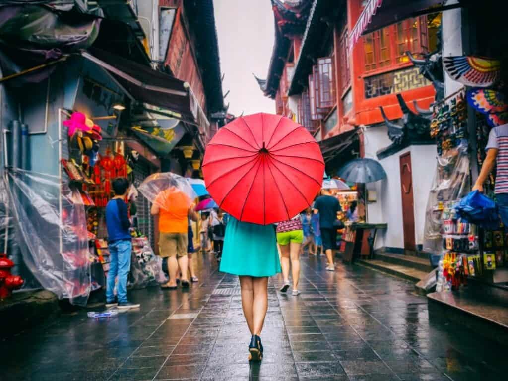 woman holding red umbrella walking through narrow alleyways of shanghai