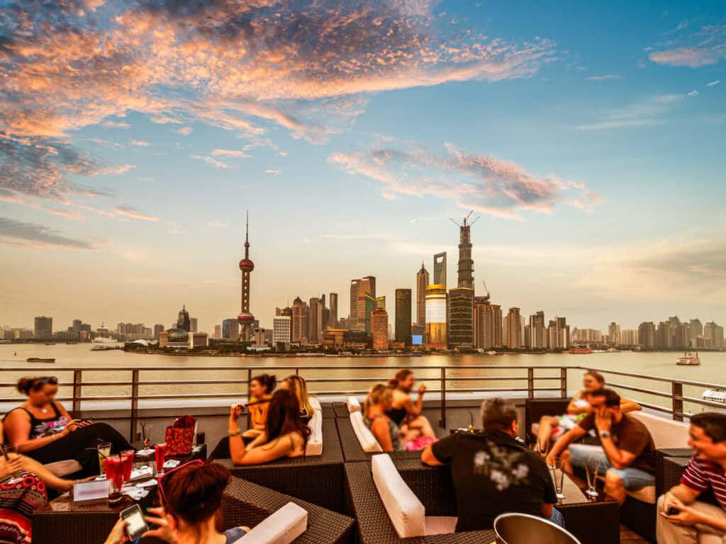 people sitting at rooftop bar with views of shanghai skyline