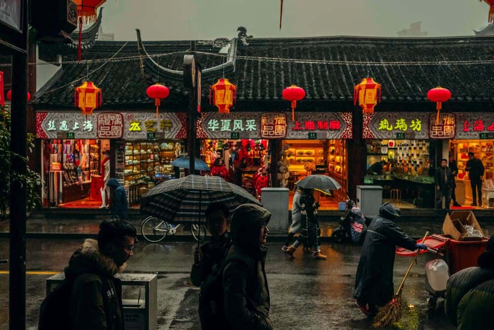 people walking past chinese buildings in the rain