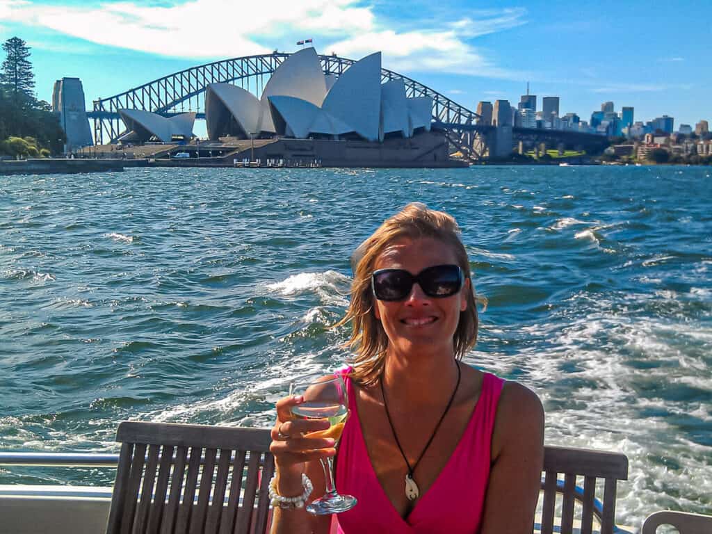 caz posing in front of sydney harbour bridge on a boat with glass of wine