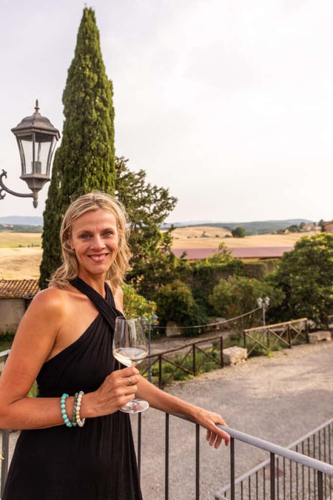 caz holding glass of wine smiling with countryside view behind her
