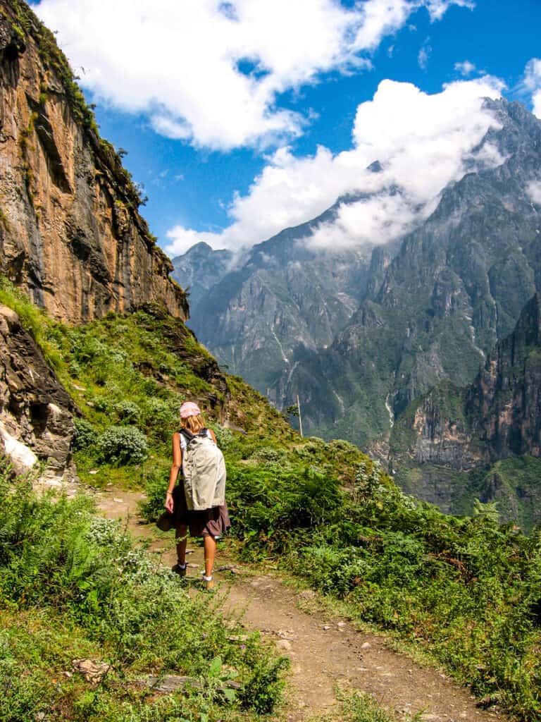 woman walking on trail beside steep mountains