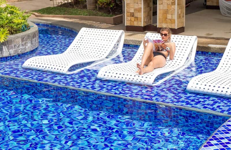 woman sitting on pool chair in water reading magazine