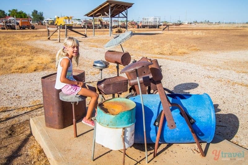 young girl sitting at drum kit made from garbage bins and scrap metal