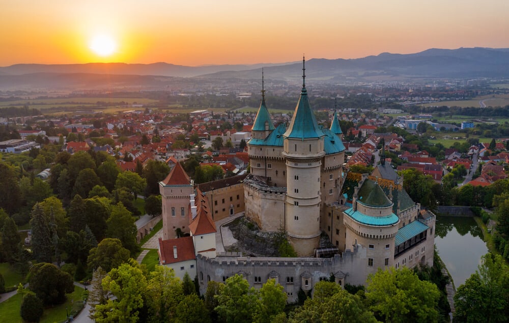 Bojnice Castle on the hill with town in valley below and orange sunset