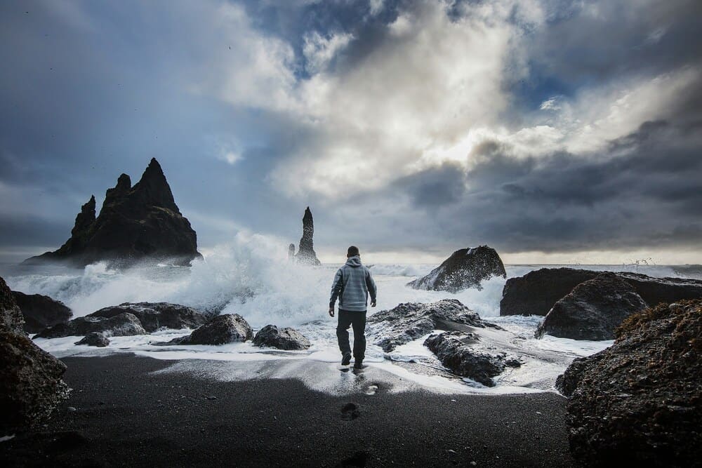 person standing on Reynisfjara Black Sand Beach looking at waves crashing into rocks
