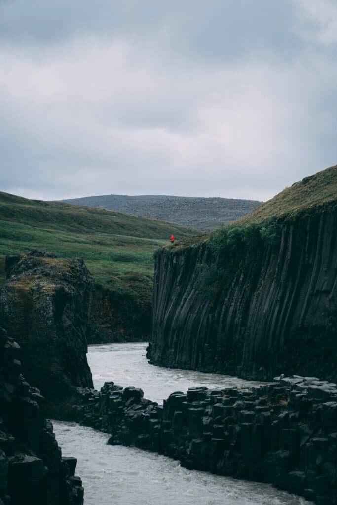 person standing on cliff looking into Studlagil Basalt Canyon