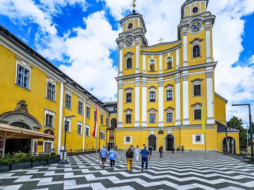 people walking across black and white tiled path to yellow basilica