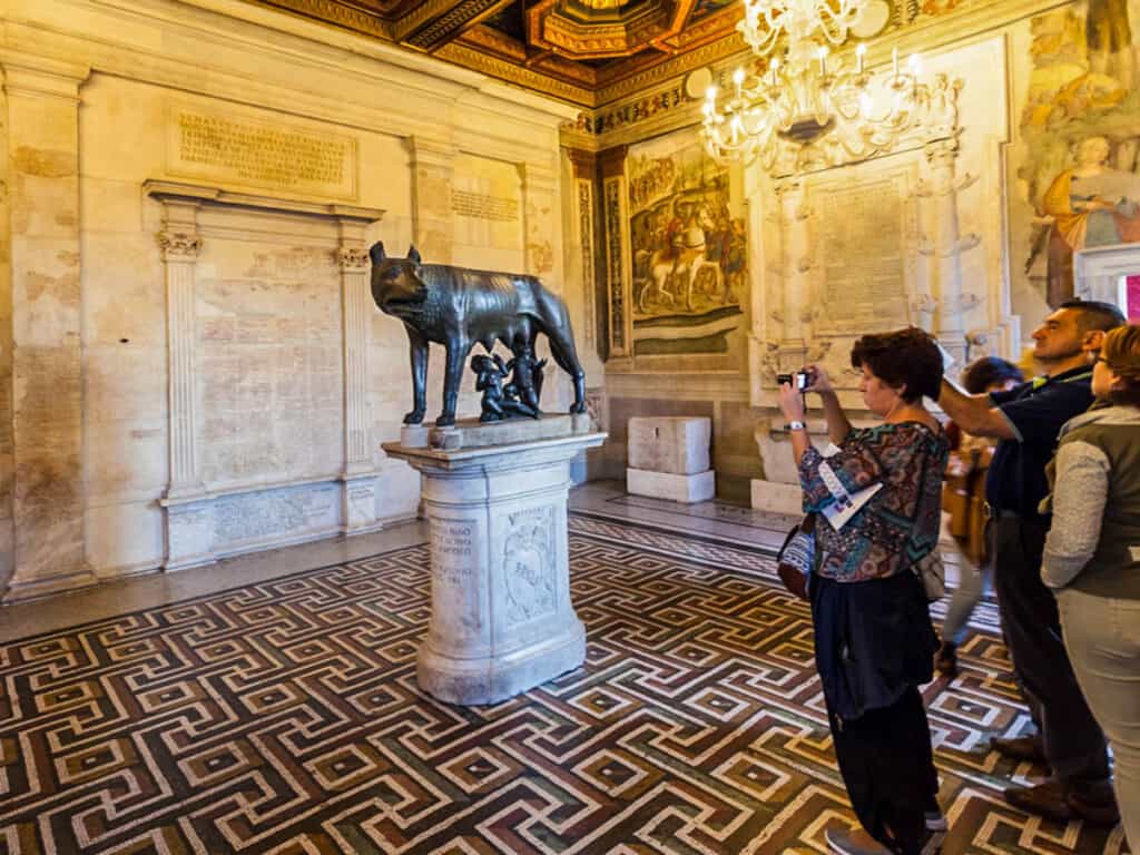 tourists in room of Capitoline Museums taking photo of capitoline wolf