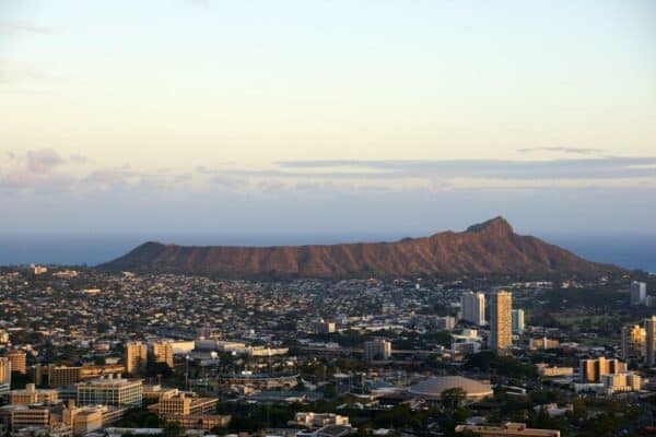 The city of Honolulu from Diamond head to Manoa with Kaimuki, Kahala, and oceanscape visible on Oahu on a nice day at dusk viewed from high in the mountains with tall trees in the foreground. Seen from Round Top Drive Lookout. May 17, 2015.