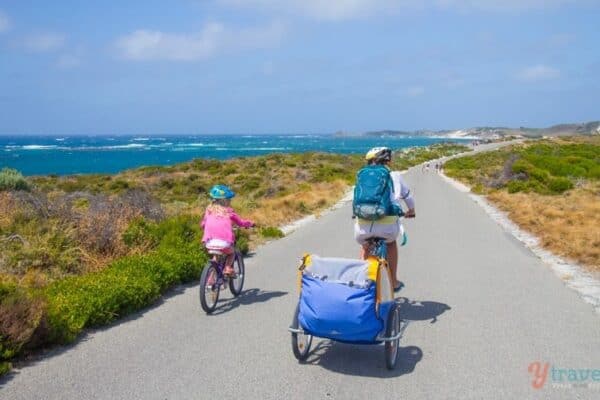 people bike riding on a road next to the ocean